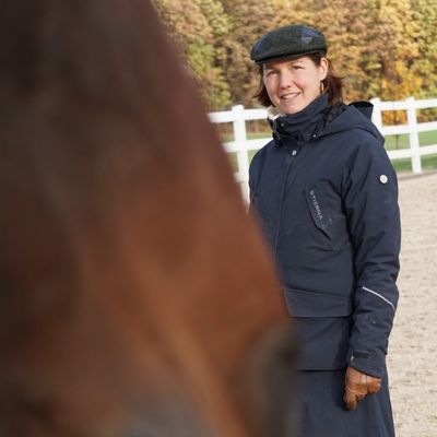 Reiterin beim Pferdetraining im Freien, lächelnd und in wetterfester Kleidung.